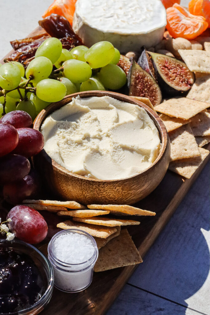 ricotta vegan cheese in a bowl surrounded by grapes and fruit. 