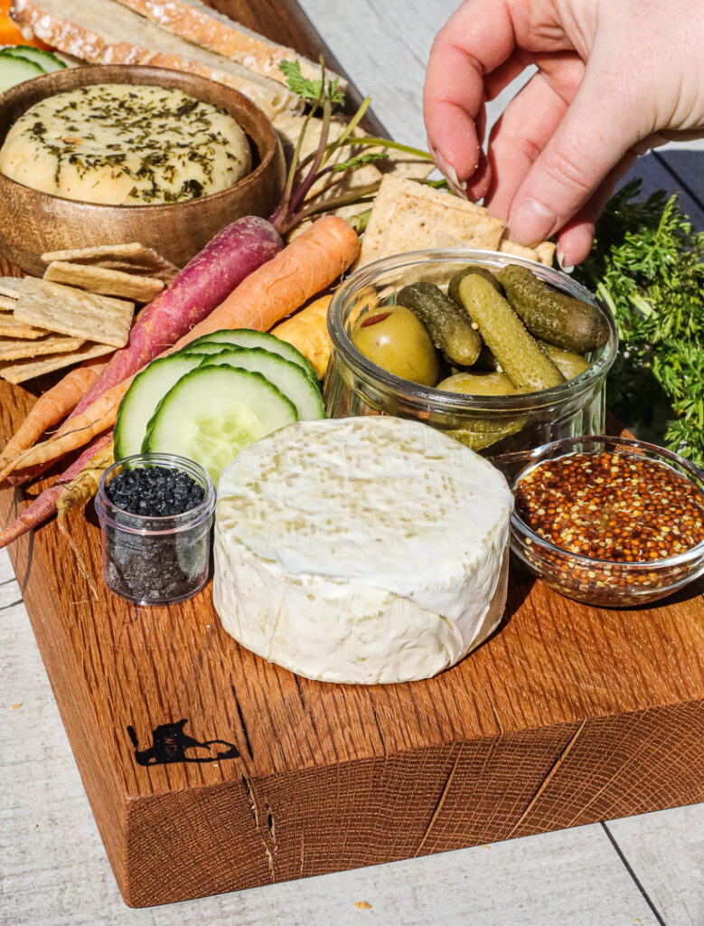 hand reaching to grab a cracker from a cheese board that has carrots, mustard, salt, and vegan cheese.